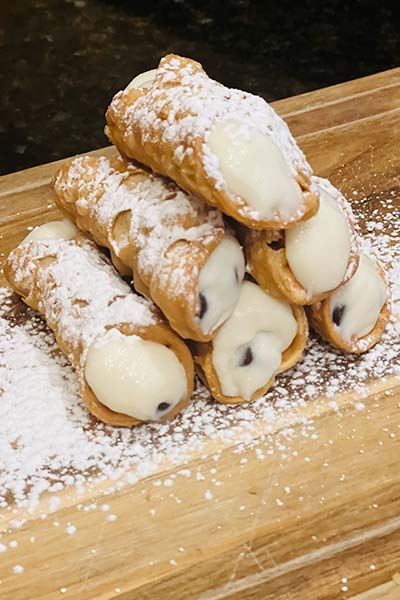 A stack of cannoli from Carini Italian Restaurant Bar Richmond Virginia, dusted with powdered sugar.
