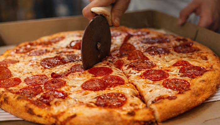 A hand slices pepperoni pizza at Carini Italian Restaurant Bar in Richmond, Virginia.