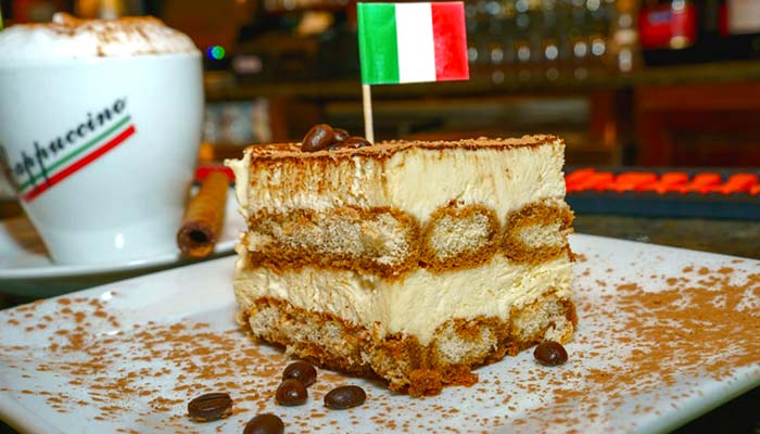 A slice of tiramisu at Carini Italian Restaurant Bar, Richmond Virginia, with coffee behind.